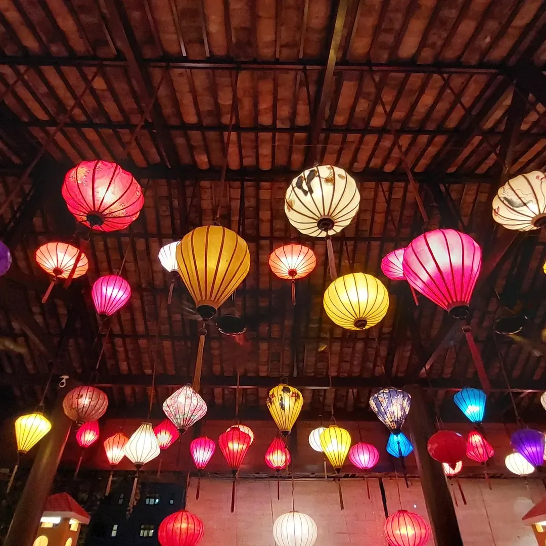 Colourful silk lanterns hanging from a wooden ceiling at night